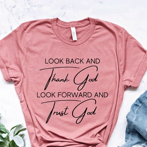 May include: A dusty rose t-shirt with the text "Look back and thank God, look forward and trust God" in black lettering.
