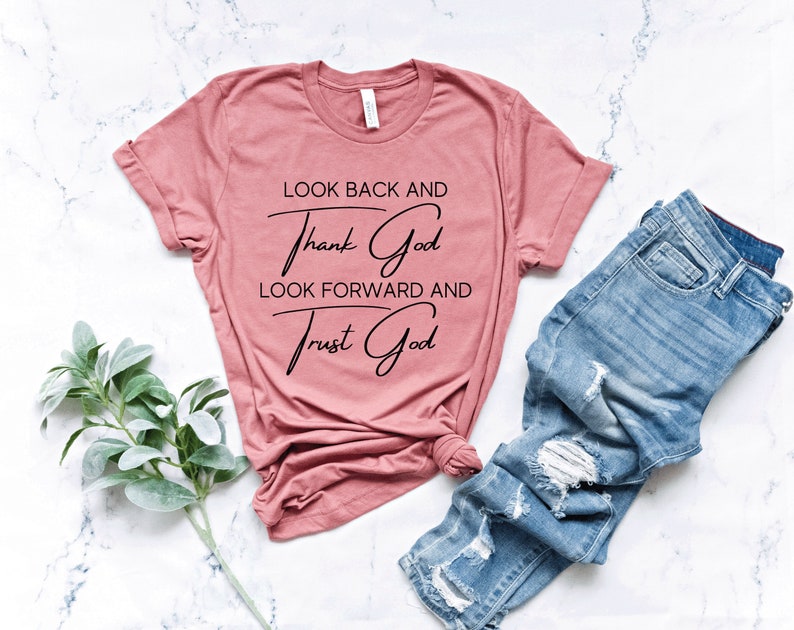 May include: A dusty rose t-shirt with the text "Look back and thank God, look forward and trust God" in black lettering.