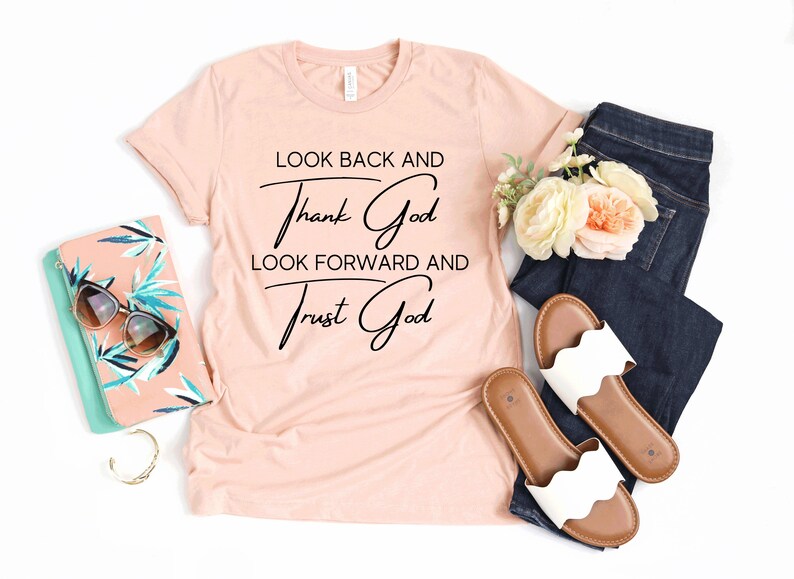 May include: A peach-colored t-shirt with the text "Look back and thank God, look forward and trust God" in black cursive lettering.