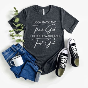 May include: A dark gray t-shirt with the text "Look back and thank God, look forward and trust God" in white lettering.