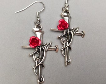May include: A pair of silver earrings with a cross design and a red rose on each cross.