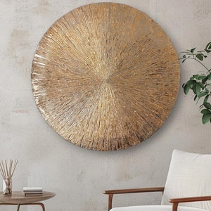 May include: A large, round, gold-toned wall decor with a textured, sunburst design. The decor is hanging on a light gray wall.