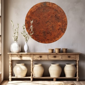 Può includere: Un decoro da parete circolare e rustico con una superficie testurizzata di colore marrone arancione. Il decoro è appeso a una parete beige chiaro sopra un tavolo console in legno con quattro cassetti e tre cesti intrecciati.