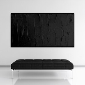 Puede incluir: Una pintura abstracta en blanco y negro cuelga sobre un banco de cuero negro con un dise&ntilde;o capiton&eacute;. El banco tiene un marco de metal plateado y se encuentra sobre un suelo blanco.