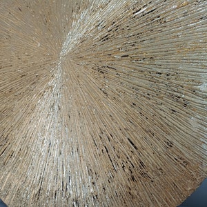 May include: A round, gold-colored wall decor with a textured, sunburst design. The surface is covered in raised lines that radiate outward from the center.