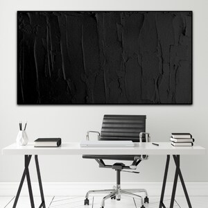 Puede incluir: Un espacio de oficina en blanco y negro con una pintura abstracta texturizada negra colgada en la pared sobre un escritorio blanco con una silla de oficina negra.