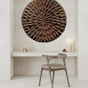 May include: A brown circular wall art piece with a textured, flower-like design hangs above a white desk with a wooden chair.