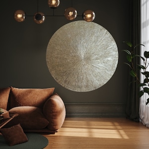 May include: A large, round, silver wall decor with a textured, radial pattern. The decor is hanging on a dark gray wall in a room with a brown leather couch.