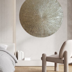 May include: A large, round, metallic wall decor with a textured, sunburst design. The decor is a light gold color and has a raised center.