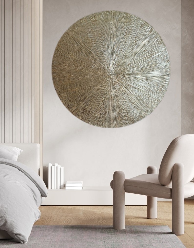 May include: A large, round, metallic wall decor with a textured, sunburst design. The decor is a light gold color and has a raised center.