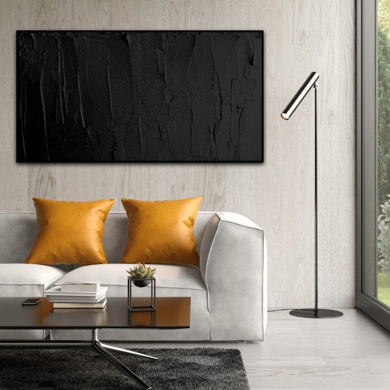 Puede incluir: Un interior de sala de estar con un sof&aacute; blanco, dos almohadones de color mostaza, una pintura abstracta en blanco y negro, una l&aacute;mpara de pie negra y una mesa de caf&eacute; con una peque&ntilde;a planta en maceta.