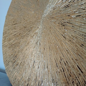 May include: A round, gold-toned wall decor with a textured, radial pattern. The surface is covered in small, raised lines that radiate outward from the center.