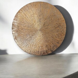 May include: A round, gold-colored wall decor with a textured, sunburst design.