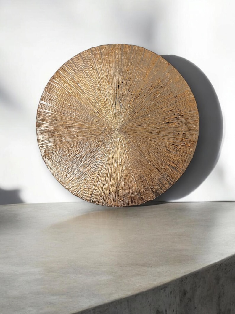 May include: A round, gold-colored wall decor with a textured, sunburst design.