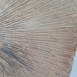 May include: A close-up of a textured, metallic silver wall art piece with a fan-like design. The surface is textured with raised lines that create a dimensional effect.
