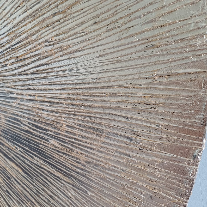 May include: A close-up of a textured, metallic silver wall art piece with a fan-like design. The surface is textured with raised lines that create a dimensional effect.