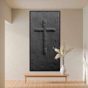 Peut inclure: Une peinture abstraite en noir et blanc d'une croix sur un fond textur&eacute;. La peinture est encadr&eacute;e en noir et est accroch&eacute;e &agrave; un mur beige au-dessus d'un banc en bois.