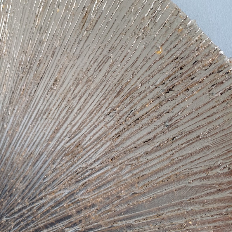 May include: Close-up of a silver metallic wall art piece with a textured, fan-like design. The surface has a subtle shimmer and a raised, layered pattern.