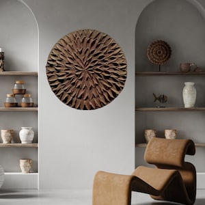 May include: A brown circular wall art piece with a textured, flower-like design. The art is hanging on a white wall in a room with a brown leather chair.