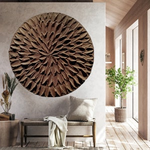 May include: A large, round, brown wall art piece with a textured, flower-like design. The art is hanging on a light gray wall in a modern living room.