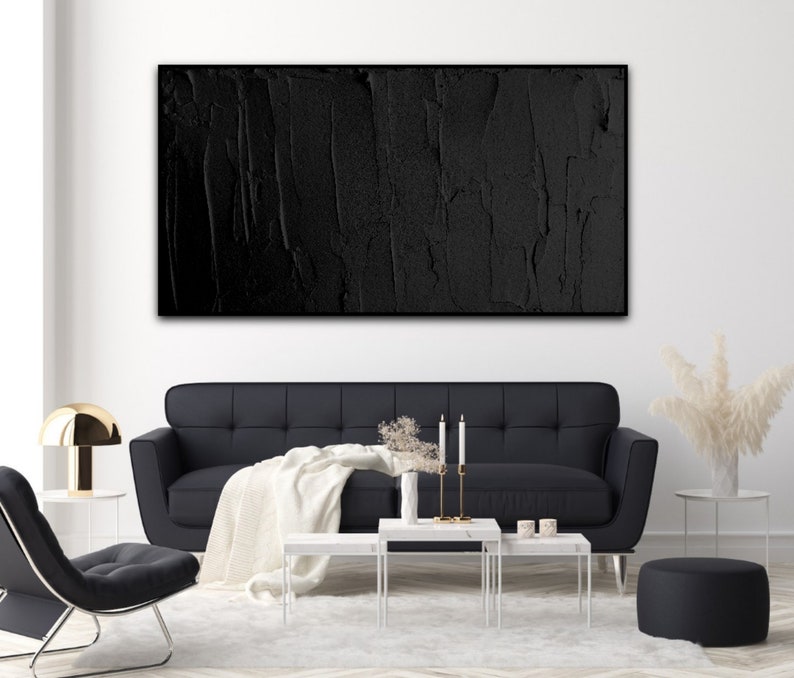 Puede incluir: Una pintura abstracta en blanco y negro con una superficie texturizada cuelga de una pared blanca sobre un sof&aacute; negro y mesas de caf&eacute; blancas.