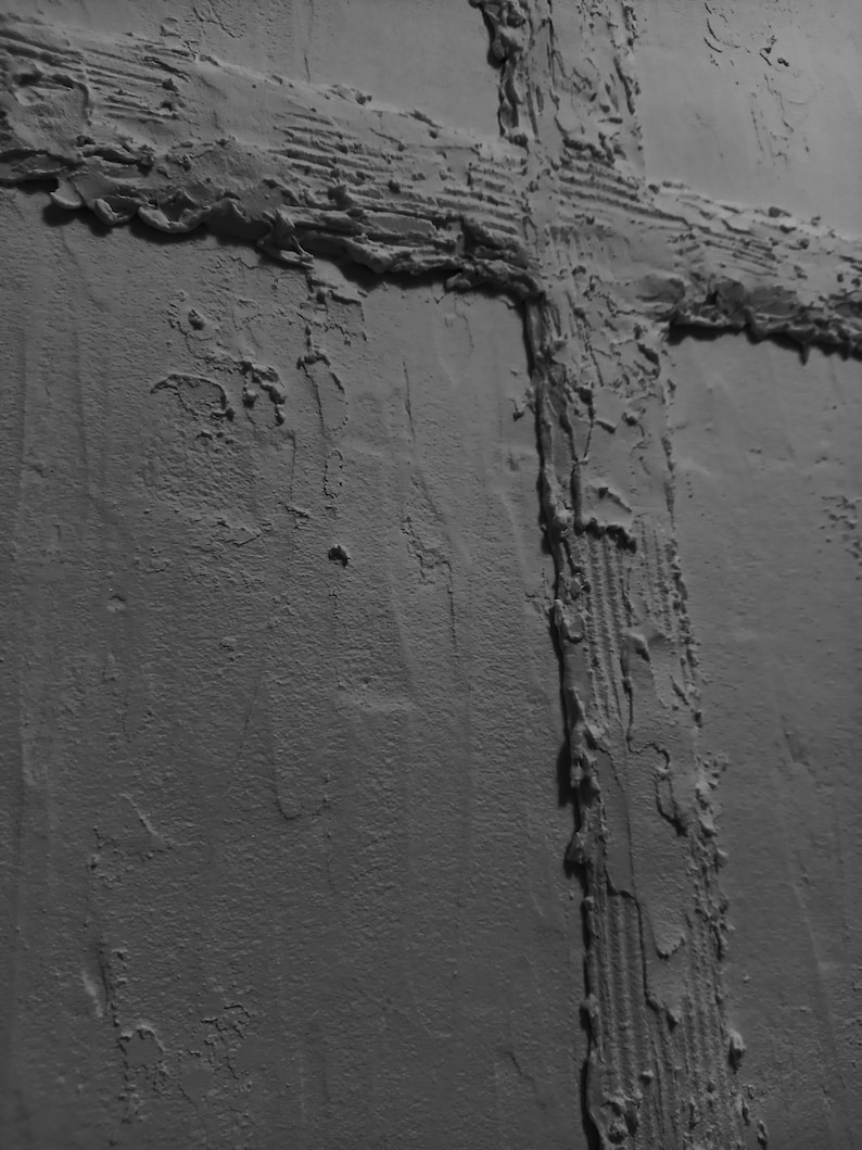 Peut inclure: Gros plan sur un mur gris textur&eacute; avec un motif de croix en relief. La croix est faite du m&ecirc;me mat&eacute;riau que le mur, mais elle est en relief et a une texture rugueuse.