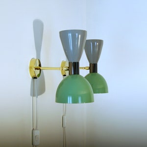 May include: A pair of wall-mounted lamps with green and gray shades. The lamps have a brass arm and a black base.