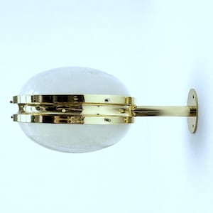 May include: A wall-mounted light fixture featuring two clear, textured glass globes held together by a polished brass center band. A matching brass arm extends from the center to a circular wall plate, securing the fixture to the surface.