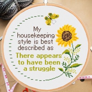 May include: White embroidery hoop with a cross-stitch design featuring a sunflower, butterfly, and the text "My housekeeping style is best described as There appears to have been a struggle."