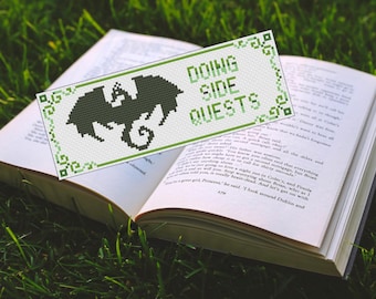 May include: A green and white bookmark with the text "DOING SIDE QUESTS" and a bat graphic, placed on an open book. The bookmark has a decorative border and is set against a backdrop of green grass.