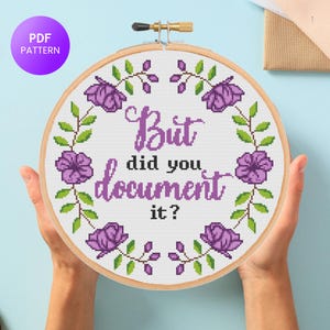 May include: A cross-stitch embroidery hoop with the text "But did you document it?" in purple. The design includes purple flowers and green leaves. A purple circle with "PDF PATTERN" is in the upper left corner.