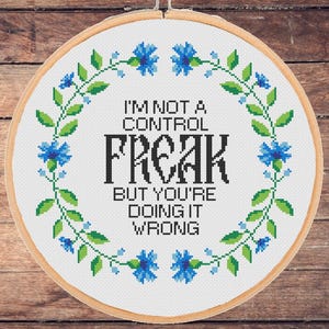 May include: A white embroidery hoop with a blue and green floral design around the edge. The text "I'm not a control freak but you're doing it wrong" is printed in black inside the hoop.