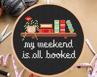 May include: A black and white cross-stitch embroidery hoop with the text "my weekend is all booked" and a pixelated image of a bookshelf with books and a potted plant.
