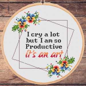 May include: White embroidery hoop with a cross-stitch design featuring the text "I cry a lot but I am so Productive it's an art" surrounded by a geometric frame and floral accents.
