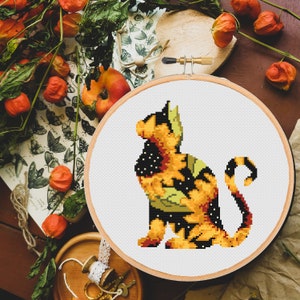 Pode incluir: Um aro de bordado de ponto cruz com um design de gato preto e amarelo. O gato está sentado com o rabo enrolado em torno do seu corpo. A pelagem do gato é estampada com manchas e redemoinhos pretos e amarelos.