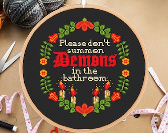 May include: A black embroidery hoop with a cross-stitch design that reads "Please don't summon Demons in the bathroom." The design is surrounded by a floral border with red, yellow, and green flowers.