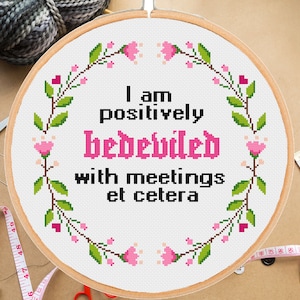 May include: A white embroidery hoop with a pink floral border and the text "I am positively bedeviled with meetings et cetera".