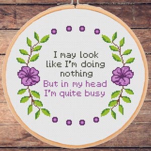 May include: White embroidery hoop with a purple floral design and the text "I may look like I'm doing nothing but in my head I'm quite busy".