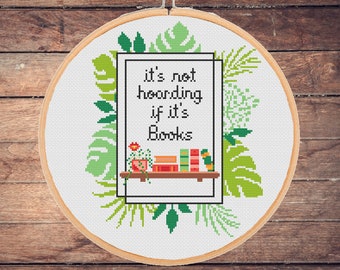 May include: A white embroidery hoop with a green and white cross-stitch design. The design features a bookshelf with books and plants, and the text "it's not hoarding if it's books".