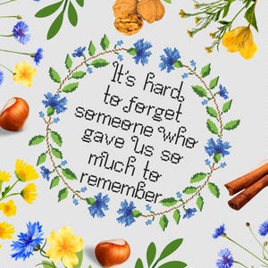 Może przedstawiać: Haftowane krzyżykiem kwiaty w formie wieńca z cytatem "Trudno zapomnieć o kimś, kto dał nam tyle do zapamiętania".