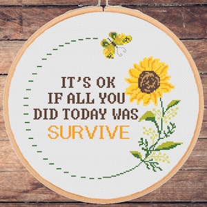 Op de afbeelding: Een witte borduurring met een gele zonnebloem en een vlinder. De tekst luidt "Het is ok&eacute; als alles wat je vandaag hebt gedaan overleven was."