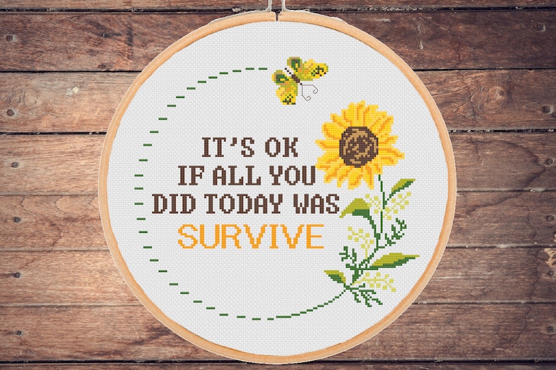 Op de afbeelding: Een witte borduurring met een gele zonnebloem en een vlinder. De tekst luidt "Het is ok&eacute; als alles wat je vandaag hebt gedaan overleven was."