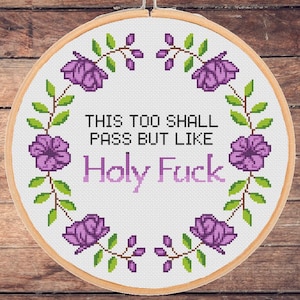 May include: A white embroidery hoop with purple flowers and green leaves around the border. The text "This too shall pass but like Holy Fuck" is stitched in the centre.