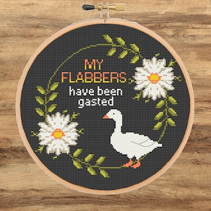 May include: A cross-stitch hoop featuring a black background with a white goose, daisies, and green leaves. The text "MY FLABBERS have been gasted" is stitched in orange and white.