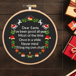 May include: A black embroidery hoop with a white background and red and green accents. The hoop features a humorous Christmas message that reads: "Dear Santa I've been good all year Most of the time Once in a while Never mind I'll buy my own stuff".