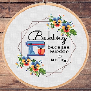 Può includere: Cerchio da ricamo a punto croce con sfondo bianco e cornice geometrica. Il disegno presenta una planetaria blu e rossa, fiori e il testo "Baking because murder is wrong."