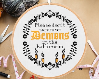 May include: A white embroidery hoop with black and yellow thread. The hoop features a cross-stitch design with the text "Please don't summon Demons in the bathroom."