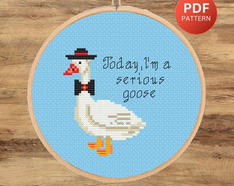 May include: Cross stitch pattern featuring a white goose wearing a black top hat and bow tie. The goose is standing on a blue background with the text "Today, I'm a serious goose".