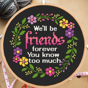 Könnte beinhalten: Ein schwarzer Stickrahmen mit einem Kreuzstich-Design, das einen Blumengirlanden und den Text "We'll be friends forever you know too much." zeigt.