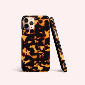 Op de afbeelding: Een smartphonehoesje met een schildpadpatroon in zwart- en amberkleuren. De hoes wordt in twee oriëntaties getoond, één plat en één schuin, waarbij de camera en de zijknoppen zichtbaar zijn. De hoes heeft een glanzende afwerking.